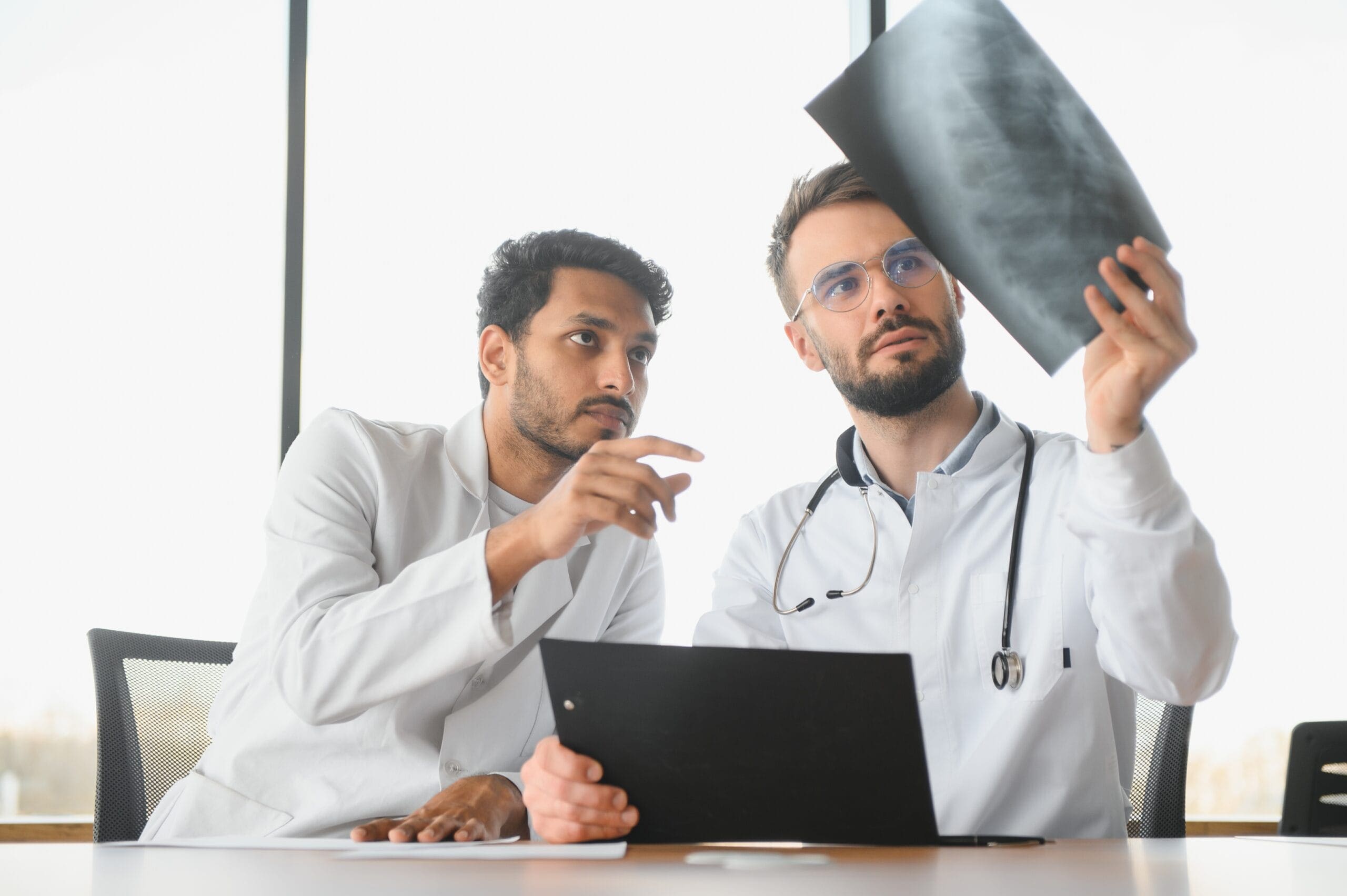 doctors reviewing an X-ray and discussing prior authorization requirements for Isoniazid Sulfate sublingual tablets for tuberculosis treatment under Caremark.