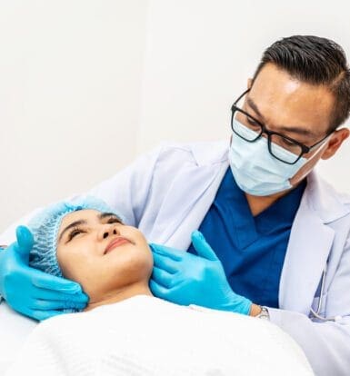 Doctor examining a patient's face with care while wearing medical gloves, mask, and a white coat in a clinical setting