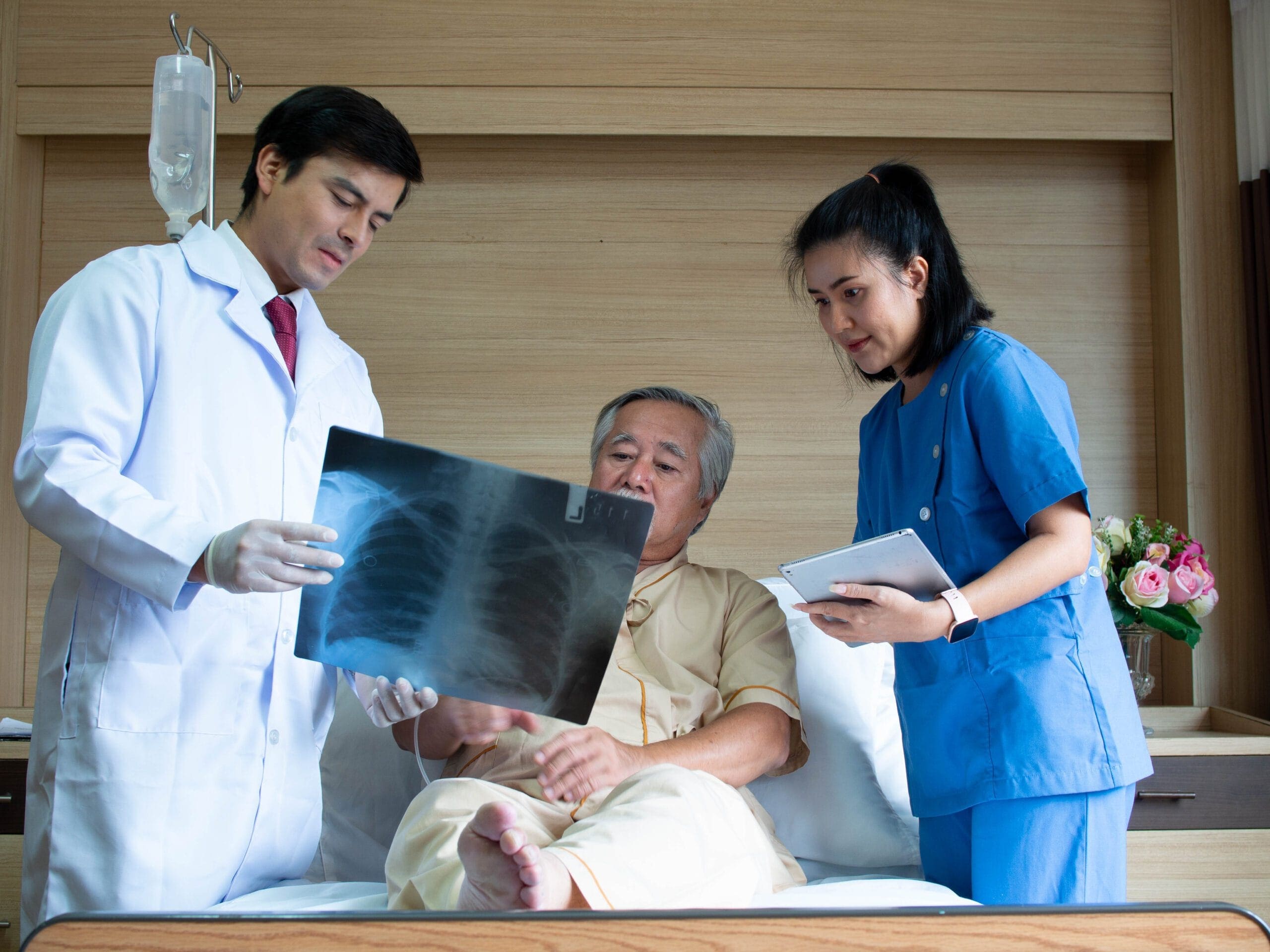 Doctor and nurse showing a chest X-ray to a patient with tuberculosis in a hospital bed, discussing treatment options.