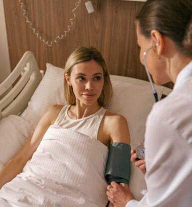 Doctor checking blood pressure of a patient in a hospital bed, symbolizing care for asthma treatment with non-formulary medication.