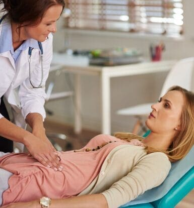 Doctor examining a patient’s abdominal area in a clinical setting, focusing on patient comfort and care