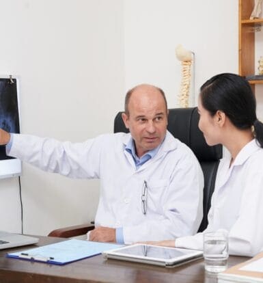 Doctor explaining X-ray to colleague during prior authorization discussion.