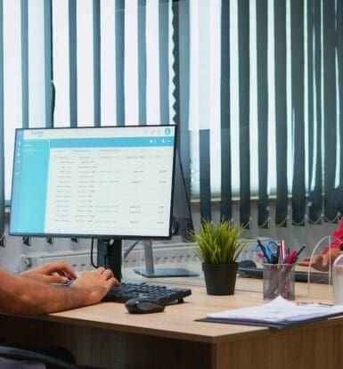 A healthcare worker and a patient in masks discussing telemedicine services in a clinic setting with patient records displayed on a screen
