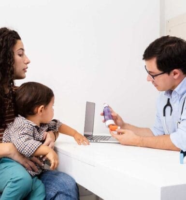 Mother and child consulting with a doctor about medication options, with doctor explaining the use of a prescription inhaler and other medications.