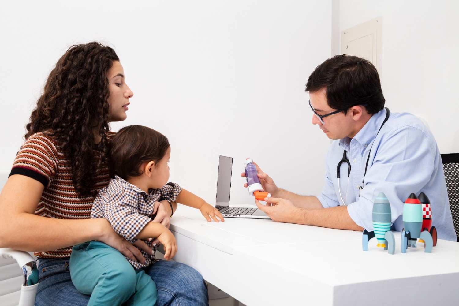 Mother and child consulting with a doctor about medication options, with doctor explaining the use of a prescription inhaler and other medications.