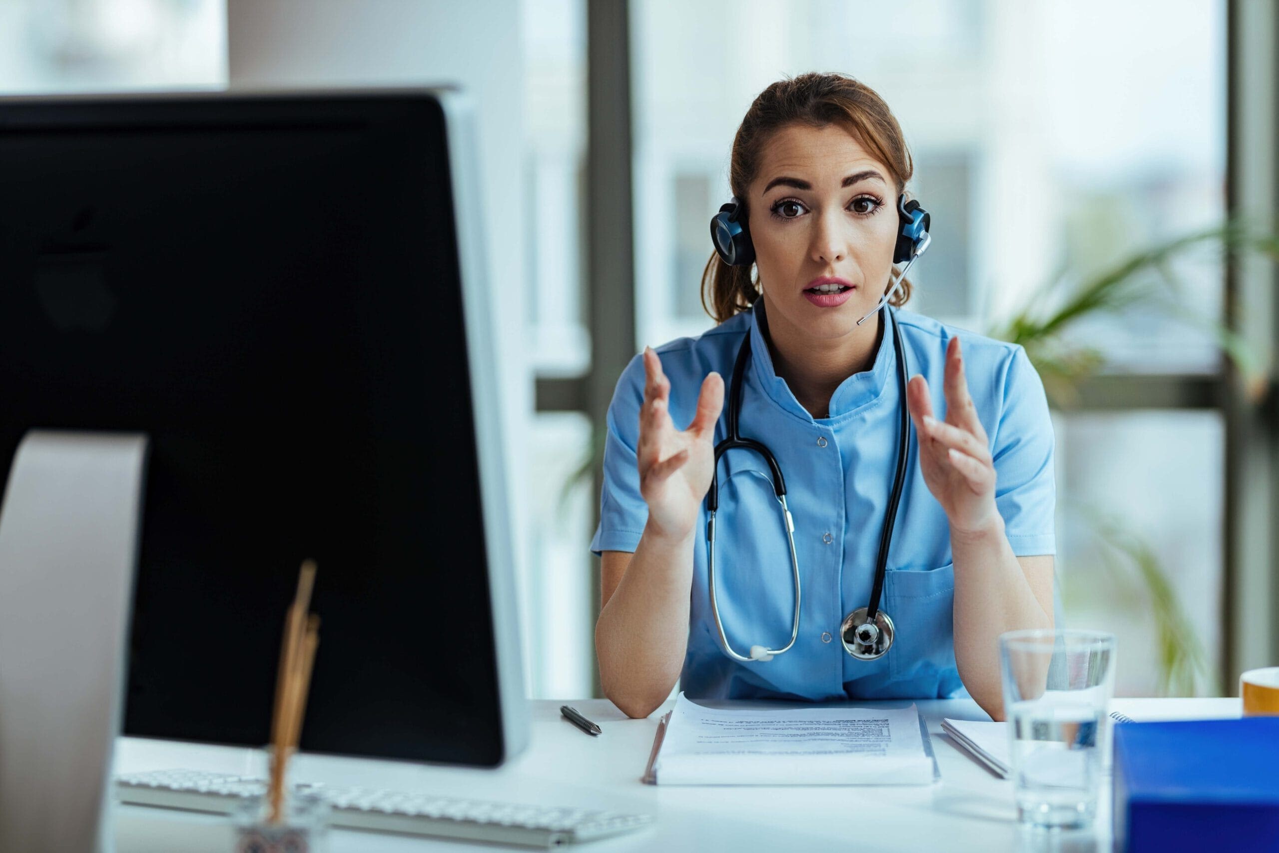Alt Text: Female healthcare professional wearing a headset and explaining telemedicine outsourcing benefits during a virtual consultation.