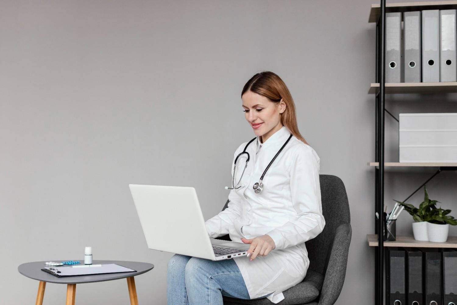 Doctor using a laptop for administrative tasks in a medical office, representing the role of virtual medical assistants vs in-house staff.