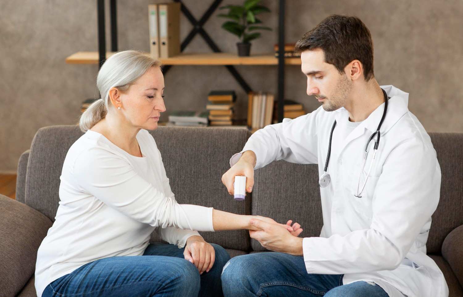 A doctor applies a treatment to a patient's arm while discussing prior authorization for a necessary medication, likely under Medicare.