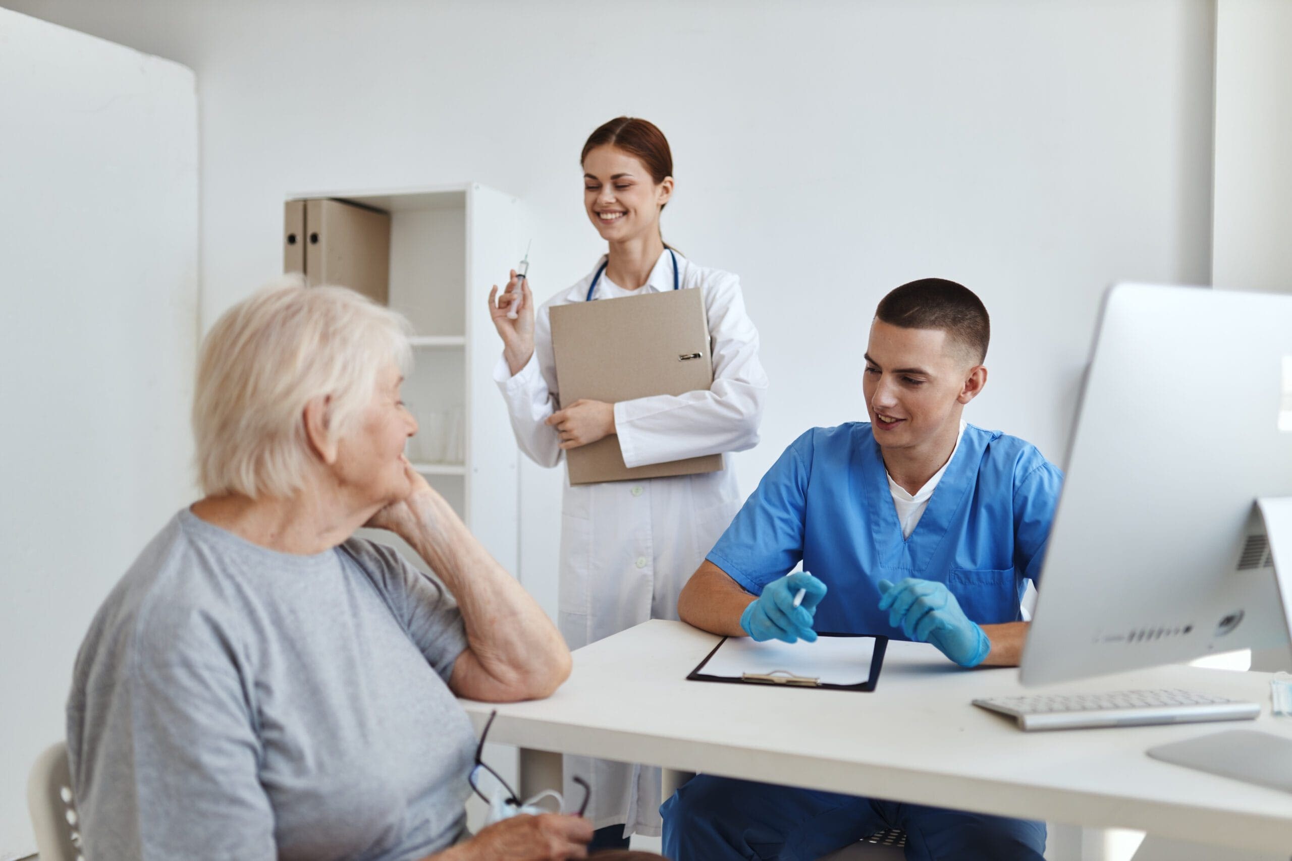 Healthcare providers discussing a patient's care plan, with a nurse and doctor smiling and reviewing documents with an elderly woman.
