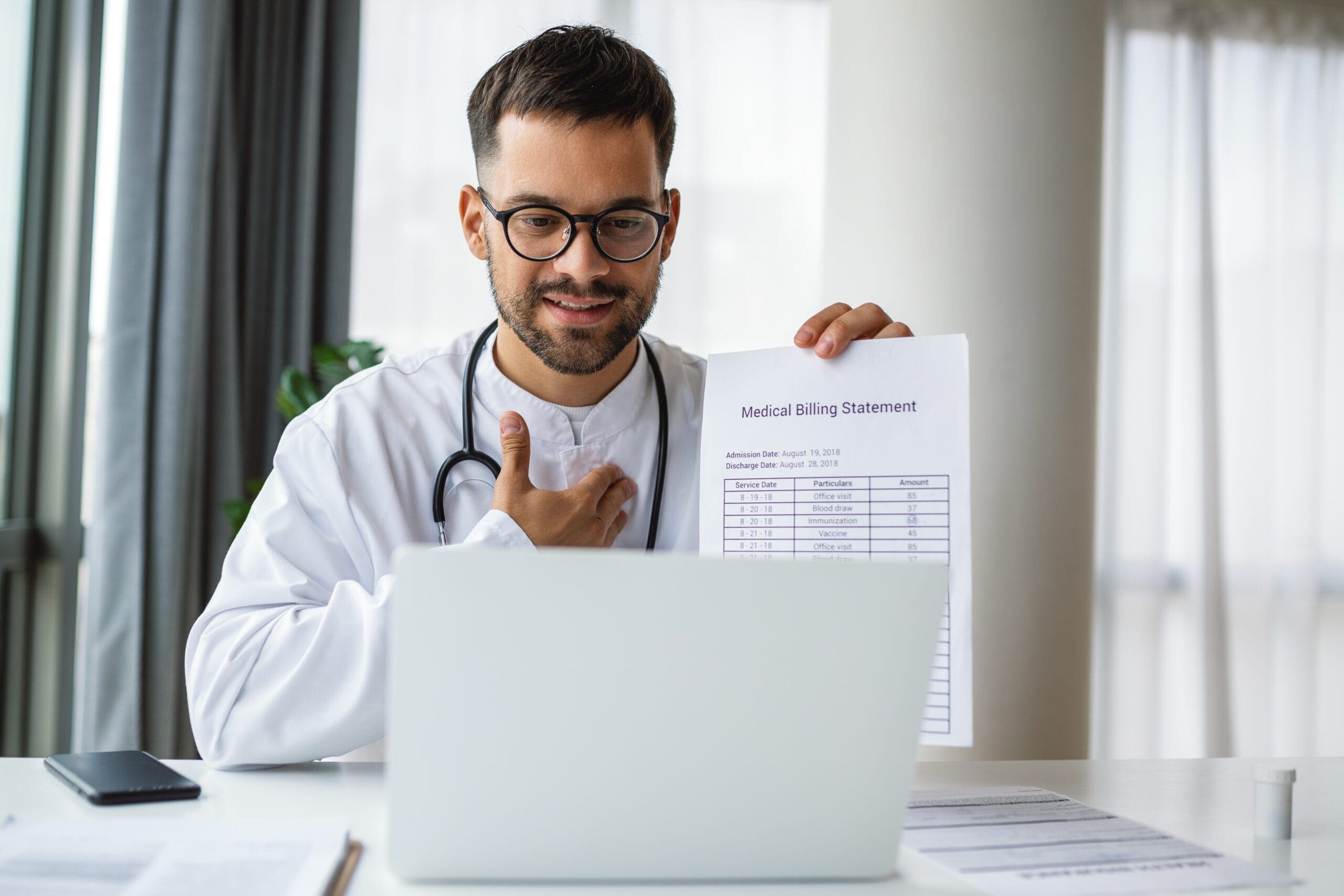 A doctor holding a medical billing statement while sitting at a desk with a laptop, explaining billing details during a virtual consultation.