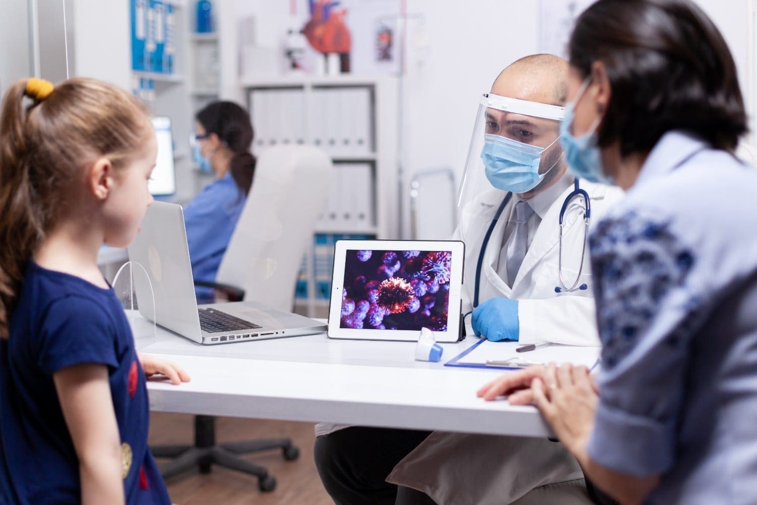 Doctor showing a digital image of a virus to a young patient and her mother, representing patient education and virtual support in healthcare.