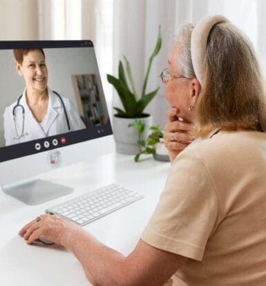 Elderly woman engaging in a telehealth appointment with a virtual medical receptionist on her desktop computer, showcasing efficient remote healthcare solutions.