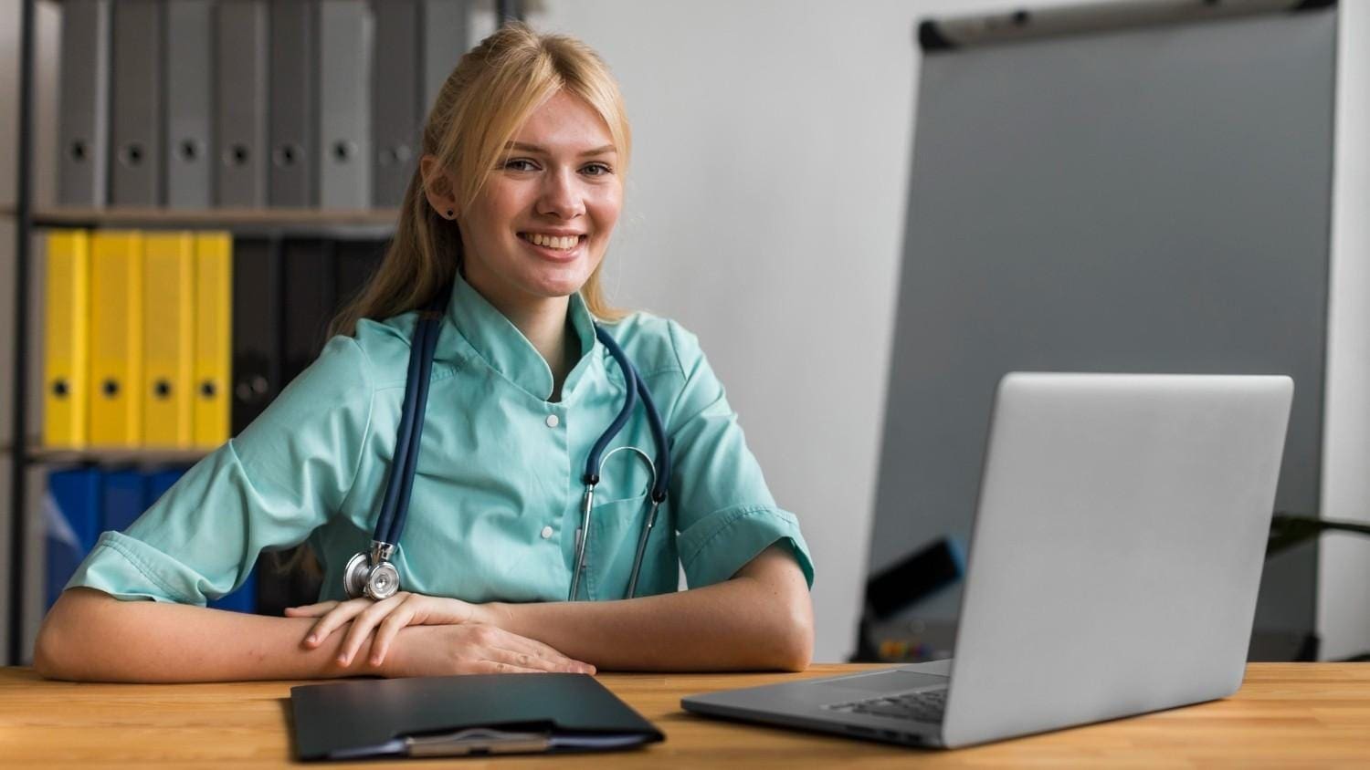 Smiling virtual medical assistant sitting at a desk with a laptop and clipboard, ready to assist telemedicine operations.