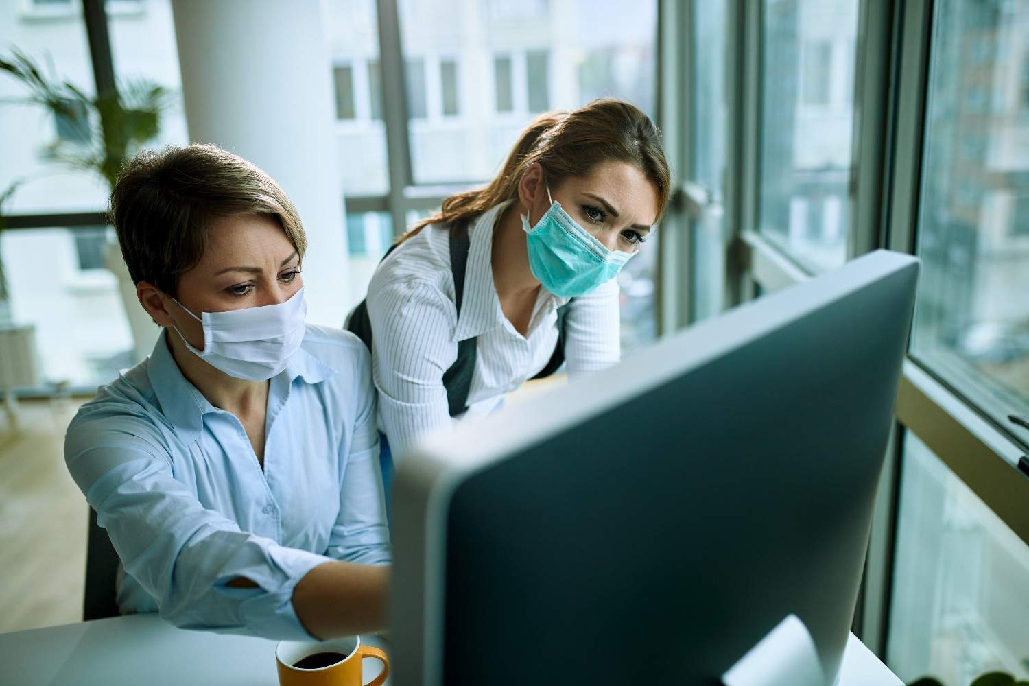 Two healthcare professionals wearing masks working on a computer, showcasing efficiency in a modern medical office.