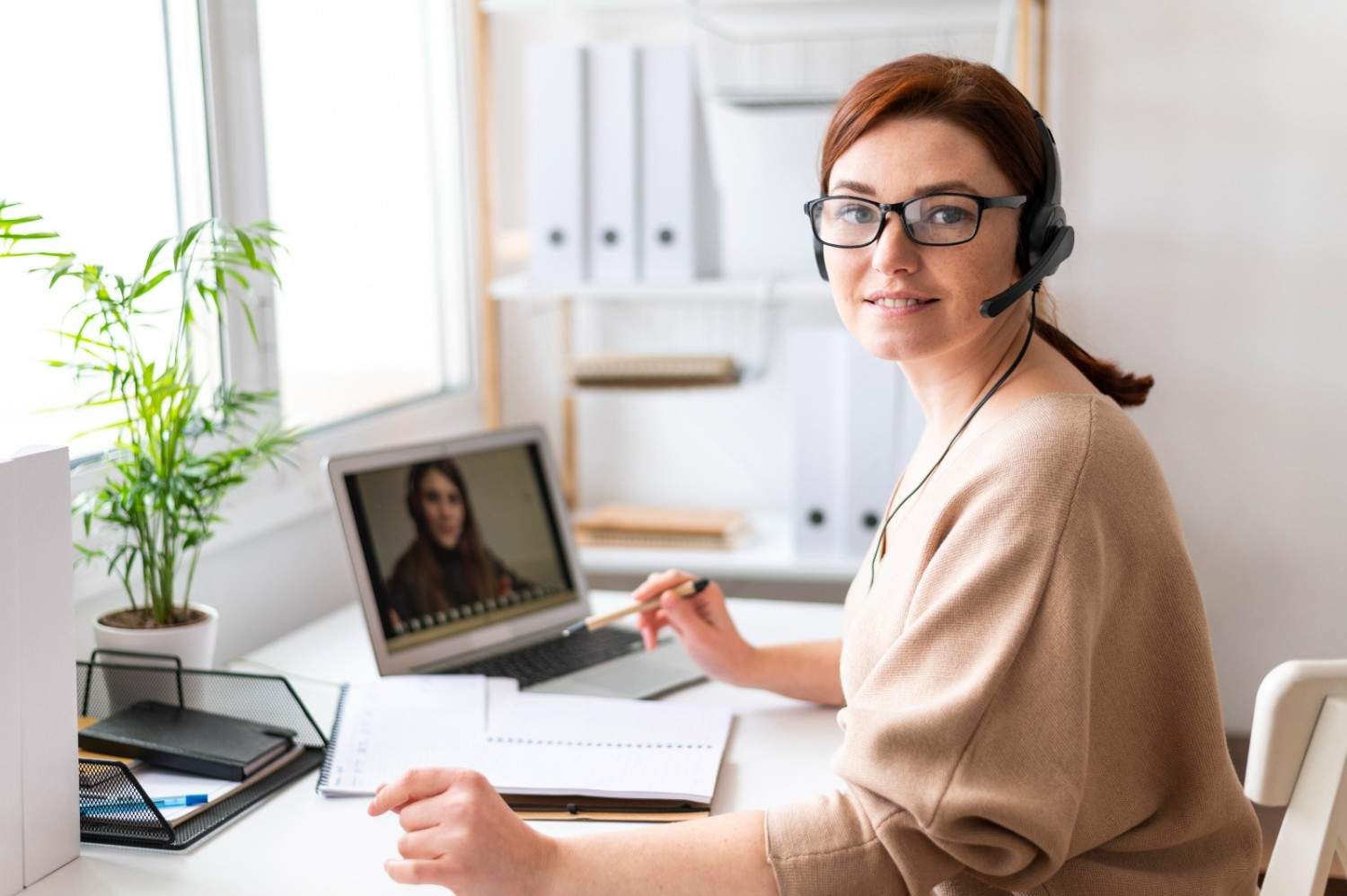 Professional virtual receptionist providing healthcare support remotely with a laptop and headset in a modern office.