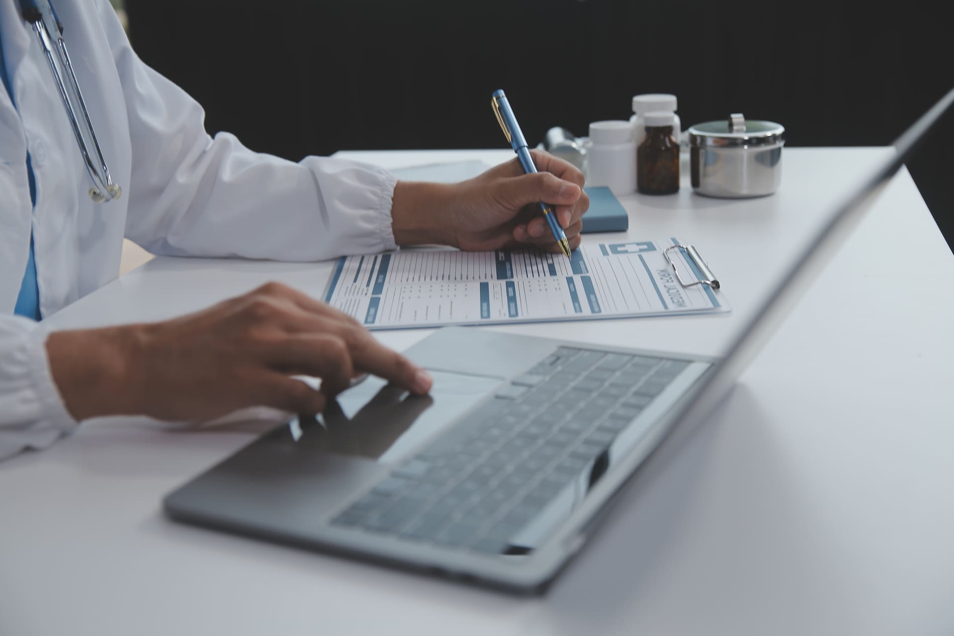 A healthcare professional filling out a prior authorization form while using a laptop for digital tracking and documentation.